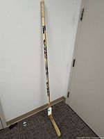 Full view of the VIC 2000 wooden hockey stick leaning against wall