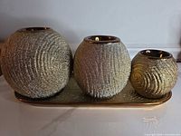 Front view of three textured gold multicolor spherical candle holders on matching tray