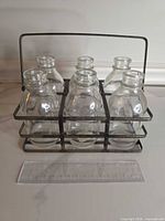Front view of six bottles seated in metal carrier with ruler for scale