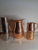 Front view of full set: pitcher centered, two stacked handled mugs on right, four stacked small cups on left, ruler for scale