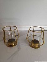 Two identical gold geometric candle holders with glass inserts