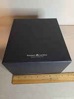 Outer black cardboard sleeve with Maurice Lacroix logo beside ruler