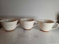Three cream stoneware cups with ruler for scale