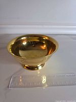 Side view of polished brass bowl with ruler indicating diameter