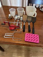 All items laid out on wooden table showing measuring cups, apple peeler, utensils and candy mold