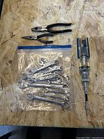 Grouped view of bagged wrenches, two pliers, and cylinder hone