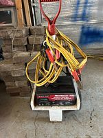 Battery charger on small dolly with bundled yellow jumper cables