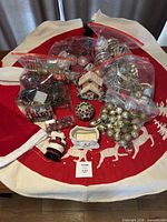 Overview of lot showing tree skirt, sleigh dish, Santa wax warmer, house ornament, candle holder and multiple bags of ornaments