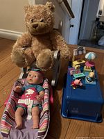 Overall lot showing baby doll in carrier, plush bear on rocker, Peppa Pig toy set on blue lid
