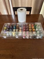 Assortment of 53 thread spools arranged in two clear cases with stabilizer roll behind
