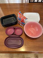 Group shot of all items: black freezer container, white freezer container, sealed shot glasses pack, purple egg poacher with lid, red popcorn maker bowl with lid