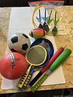 Assorted bats, balls, rackets and lawn darts on table