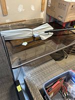 Rectangular smoked glass patio table with folded grey umbrella on top, portion of chair visible