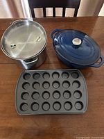 Stainless pot with lid, blue Dutch oven, mini muffin pan together on table