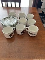 Stack of fruit motif plates beside eight matching mugs