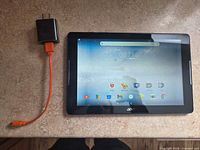 Front view of Acer Iconia One 10 tablet powered on beside charger and cable