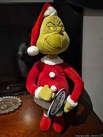 Full front view of Grinch plush holding Naughty side of sign