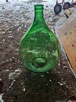 Front view of green glass demijohn showing bulbous shape, narrow neck, and overall condition
