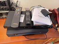 Stack showing Panasonic VCR, Philips DVD player, Magnasonic portable DVD player, two remotes, adapter, manual