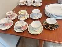 Seven teacup and saucer sets on table