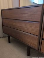 Front view of teak dresser showing three drawers and legs