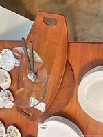 Large teak handled platter beneath round teak platter and glass salad bowl with utensils