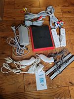 Lot overview showing Wii Mini console, AC adaptor, remotes, nunchucks, sensor bars, AV cables, dongle