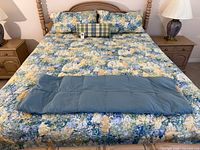 Full view of bed with floral comforter, two shams, plaid bolster, and folded quilted throw at foot