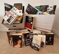 Two bankers boxes filled with assorted hardcover and paperback books, additional books displayed in front