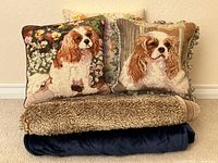 Group shot of two dog needlepoint pillows, embroidered pillow behind, faux-fur throw and navy electric blanket
