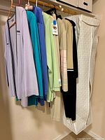 Multiple knit cardigans on hangers plus white pants in garment bag