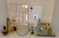 All items on shelf: assorted perfume bottles, mirrored tray, glass dish, acrylic organizer