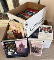 Boxes containing assorted hardcover books with several titles displayed