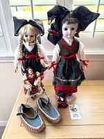 Group shot of all items: two porcelain dolls, cloth doll, plastic doll, woven shoes, stand base visible