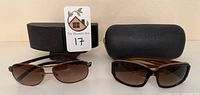 Two sunglasses with respective cases, Prada left, Chanel right
