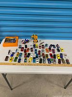 Tabletop view of entire lot showing diecast cars, Transformer figure, orange case and other toys