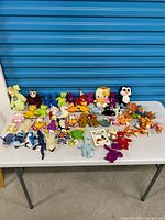 Full table view of mixed Ty Beanie Babies, other plush toys and handbook