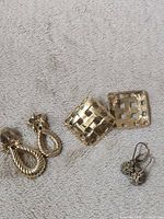 Three pairs of earrings laid out: twisted drops, lattice studs, rhinestone drops
