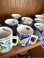 Group of seven BOPLA! porcelain mugs showing exterior artwork and handles