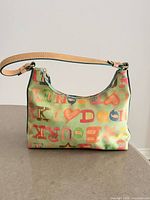 Front view of Dooney & Bourke mini shoulder bag showing multicolor alphabet print and tan leather strap