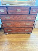 Front view of dresser showing six drawers, veneer finish, brass pulls, bun feet