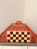 Front view of folded wooden board showing inlaid squares and carved triangular shape with handle
