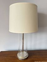 Full view of table lamp showing glass column, fabric shade, base