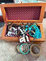 Open wooden jewelry box filled with assorted bangles and bead necklaces