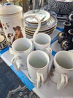 Stack of blue bird motif plates and group of Norman Rockwell mugs on table