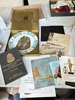 Lot overview showing plate in box, sealed book, gazette page and pamphlets