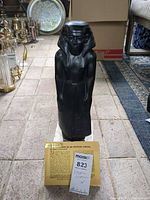 Full view of black Egyptian reproduction statue on marble base with info card visible