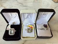Three boxed rings displayed: two pale green stone rings and one purple stone ring