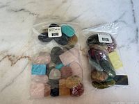 Both plastic bags of assorted polished cabochons on countertop