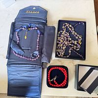 Overview of three boxed jewelry items: purple bead necklace in Stauer roll, purple drop bead necklace in black box, red bead necklace and bracelet in small box